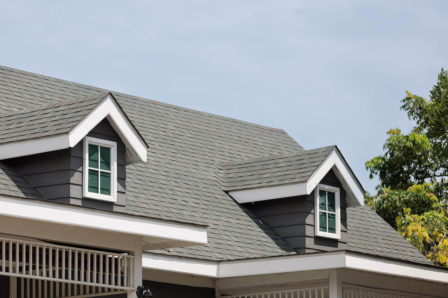 Close up of dark shingles on a residential roof. There are two dormer windows.